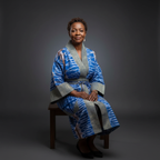 Woman wearing a blue and gray patterned robe sitting on a chair against a dark background