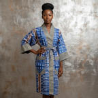 Woman wearing a blue and gray patterned robe against a textured wall.