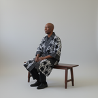 Man sitting on a wooden bench wearing a patterned robe against a plain background