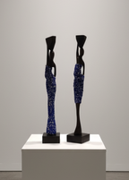 Two abstract sculptures on a white pedestal against a gray wall.