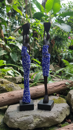 Two blue and black sculptures on a rock with a natural, green background