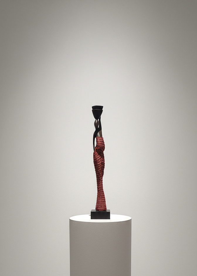 Stylized sculpture of a figure on a white pedestal against a plain background