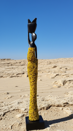 Abstract sculpture with yellow textured base and black figure on a sandy background